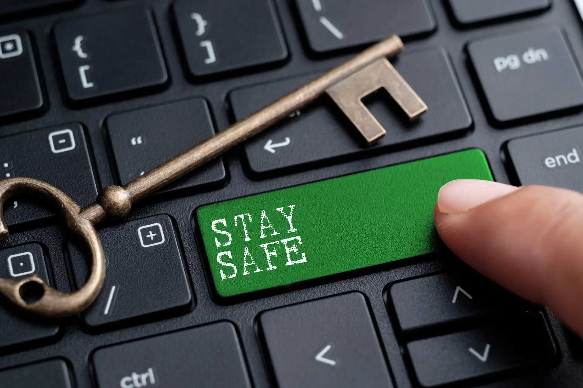 Brass key resting on a laptop keyboard above a green STAY SAFE key
